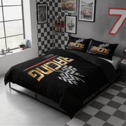 A racing-themed bedding set featuring a black duvet cover and two matching pillowcases with gold, white, and red graphics, styled on a bed in a modern gray bedroom with checkered wall accents.