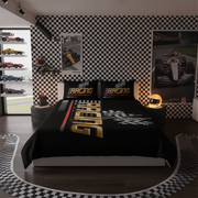 A racing-themed bedding set on a bed in a styled bedroom. The set includes a black comforter and two matching pillowcases with gold, white, and red track-inspired graphics and the word 'RACING'.
