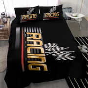 A black racing-themed bedding set including a duvet cover and two matching pillowcases, displayed on a bed in a modern bedroom setting. The design features a large gold and black 3D 'RACING' text graphic, a checkered flag motif, and a red and black stripe accent.