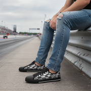Person wearing checkered sneakers sitting on a barrier at a race track.