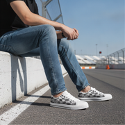 Person sitting on a concrete barrier wearing checkered sneakers and blue jeans.