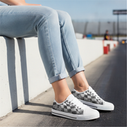 Person wearing checkered sneakers and light blue jeans sitting on a concrete ledge.