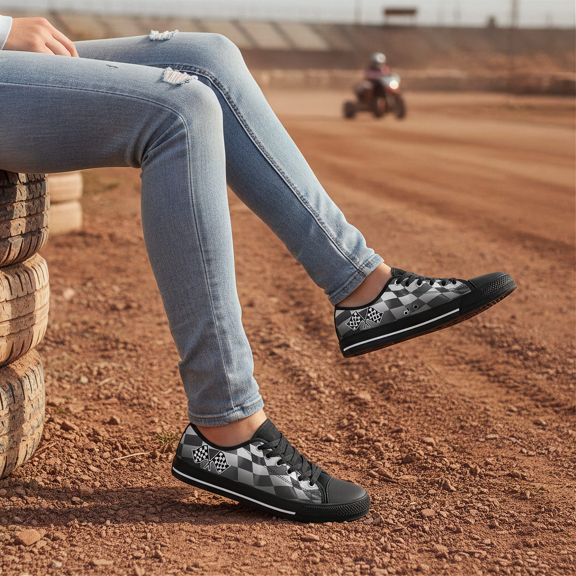 Person wearing black checkered sneakers sitting on a stack of tires on a dirt track.