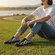 Person sitting on grass wearing checkered shoes with a scenic background