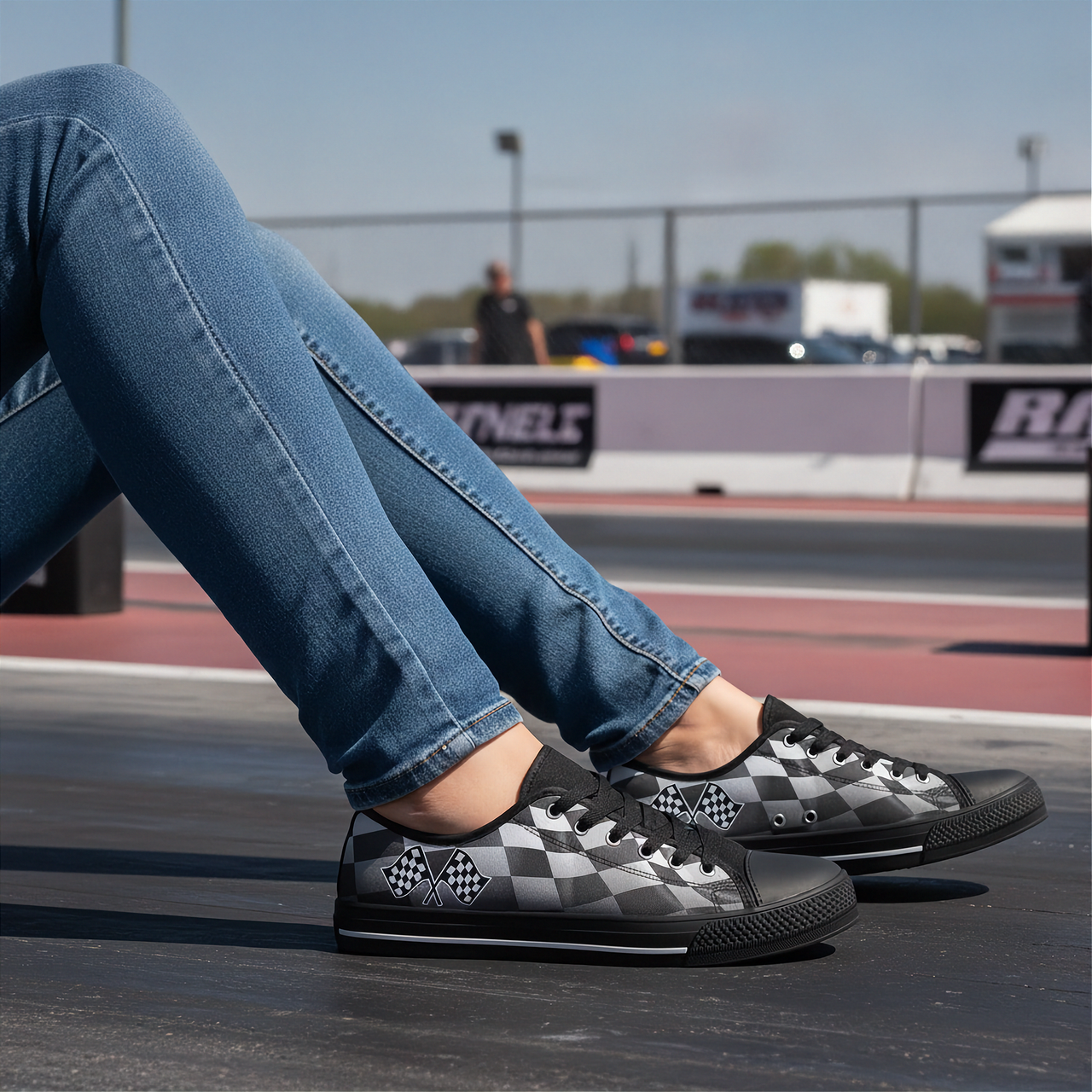 Person wearing black and gray checkered sneakers with blue jeans, sitting on a track.