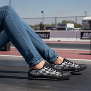 Person wearing black and gray checkered sneakers with blue jeans, sitting on a track.
