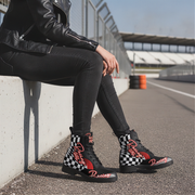 Person wearing black high-top boots with checkered pattern and 'Racing girl' text, sitting on a track.