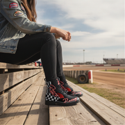 Person sitting on a wooden bench at a race track wearing checkered racing boots.