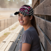 Woman wearing a checkered racing cap leaning against a wooden wall.