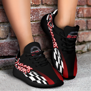 Black sneakers with red and white accents worn by a person standing against a brick wall.