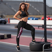 Woman in black racing girl leggings posing on a race track with cars in the background