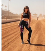 Woman in black athletic wear standing on a dirt track with a motorcycle in the background