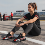 Woman sitting on a race track wearing black shoes with red and white checkered patterns.