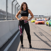 Woman in black athletic wear standing on a race track with racing cars in the background