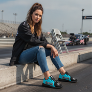 Woman sitting on a track wearing black and blue shoes with a car in the background