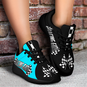 Black sneakers with blue accents and racing-themed designs worn by a person against a brick wall.
