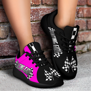 Black sneakers with pink and white designs worn by a person against a brick wall.