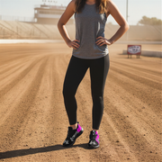 Woman in athletic wear standing on a dirt track with hands on hips wearing black and pink racing girl sneakers
