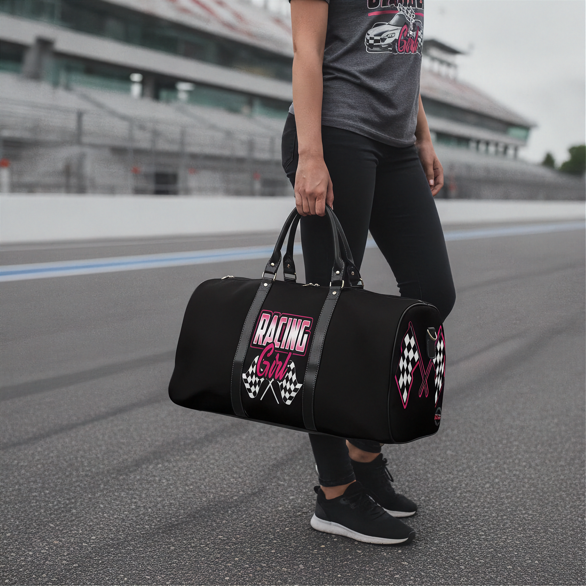 Woman holding a black duffel bag with 'Racing Girl' text on a race track.