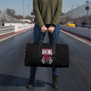 Person holding a black duffel bag with 'Racing Girl' text on a race track.