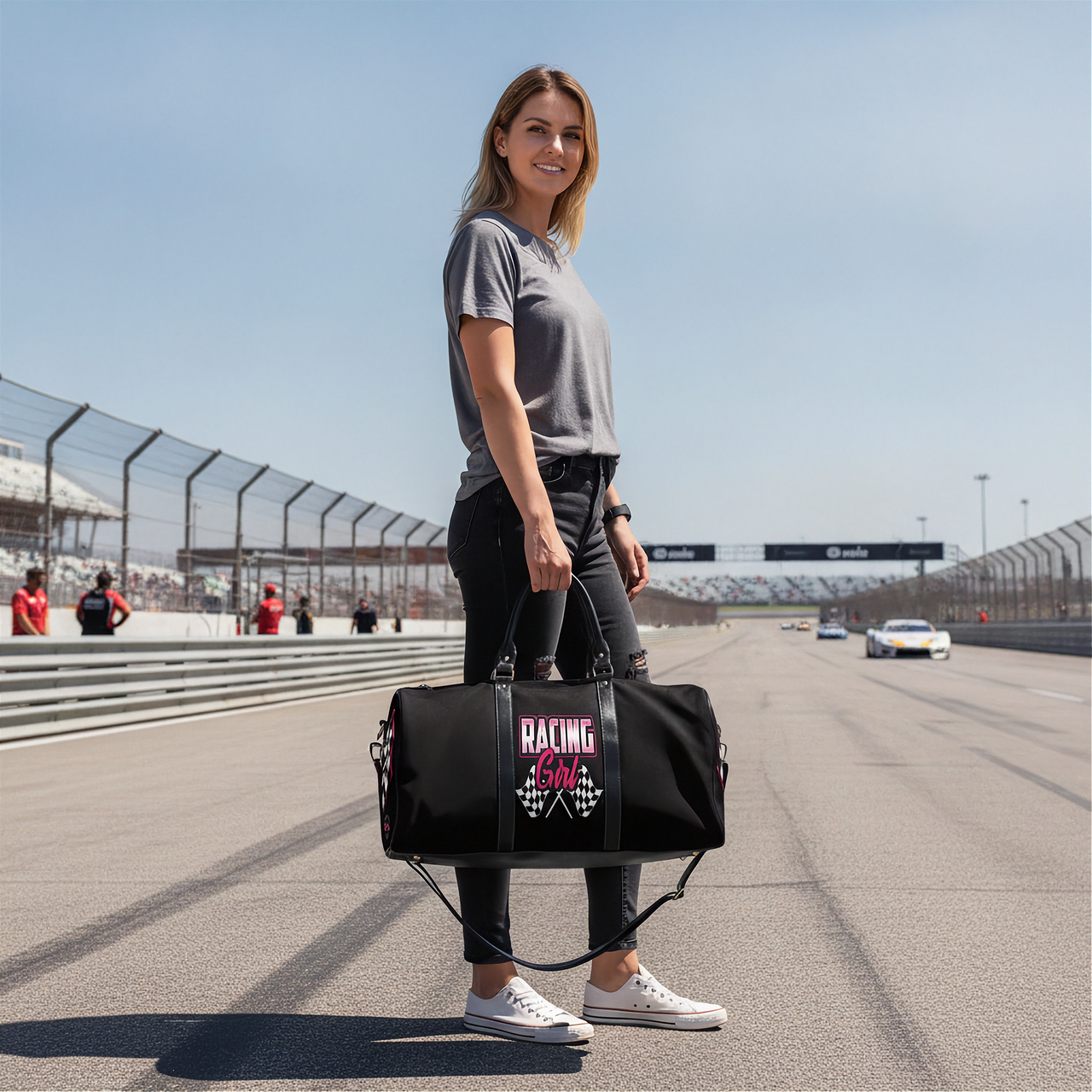 Woman holding a black duffel bag with 'Racing Girl' design on a race track.
