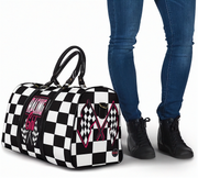 Black and white checkered bag with racing design next to a person wearing blue jeans and black shoes.