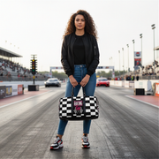 Woman holding a travel bag with a pink racing girl and checkered flag design at a drag race track, customizable text.