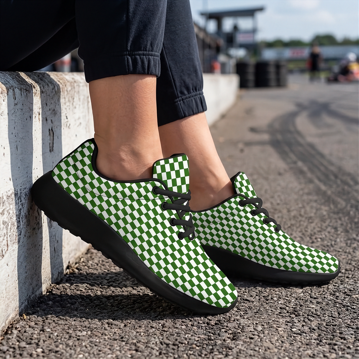 A person wearing green and white checkered sneakers with black soles and laces, standing on a paved surface next to a concrete barrier.