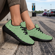 A person sitting on a street curb wearing green and white checkered sneakers with black soles and black laces, with a blurred road and cars in the background.
