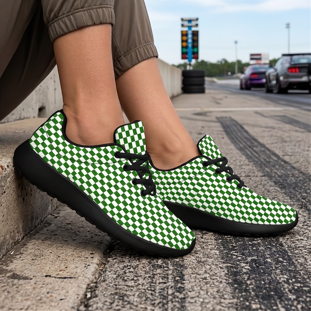 A person sitting on a street curb wearing green and white checkered sneakers with black soles and black laces, with a blurred road and cars in the background.