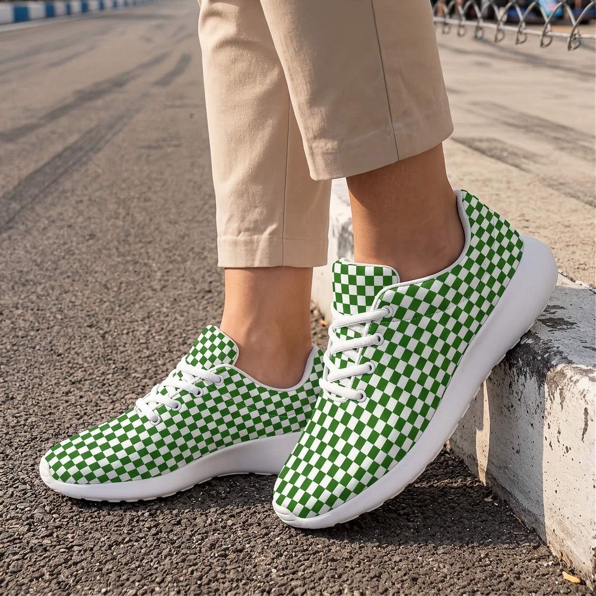 A person wearing beige pants and green-and-white checkerboard sneakers, standing on asphalt next to a concrete curb.