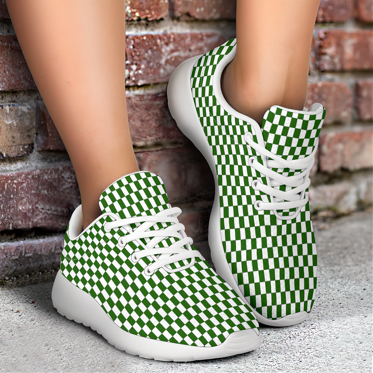 A pair of green and white checkerboard sneakers worn on a person's feet, standing on a concrete surface against a brick wall background.