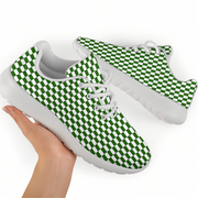 A pair of low-top sneakers with a green and white checkerboard pattern on the uppers and white soles, shown with one shoe being held by a hand against a plain white background.