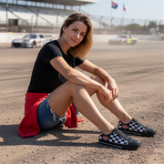 Woman sitting on a race track wearing black and white checkered shoes.
