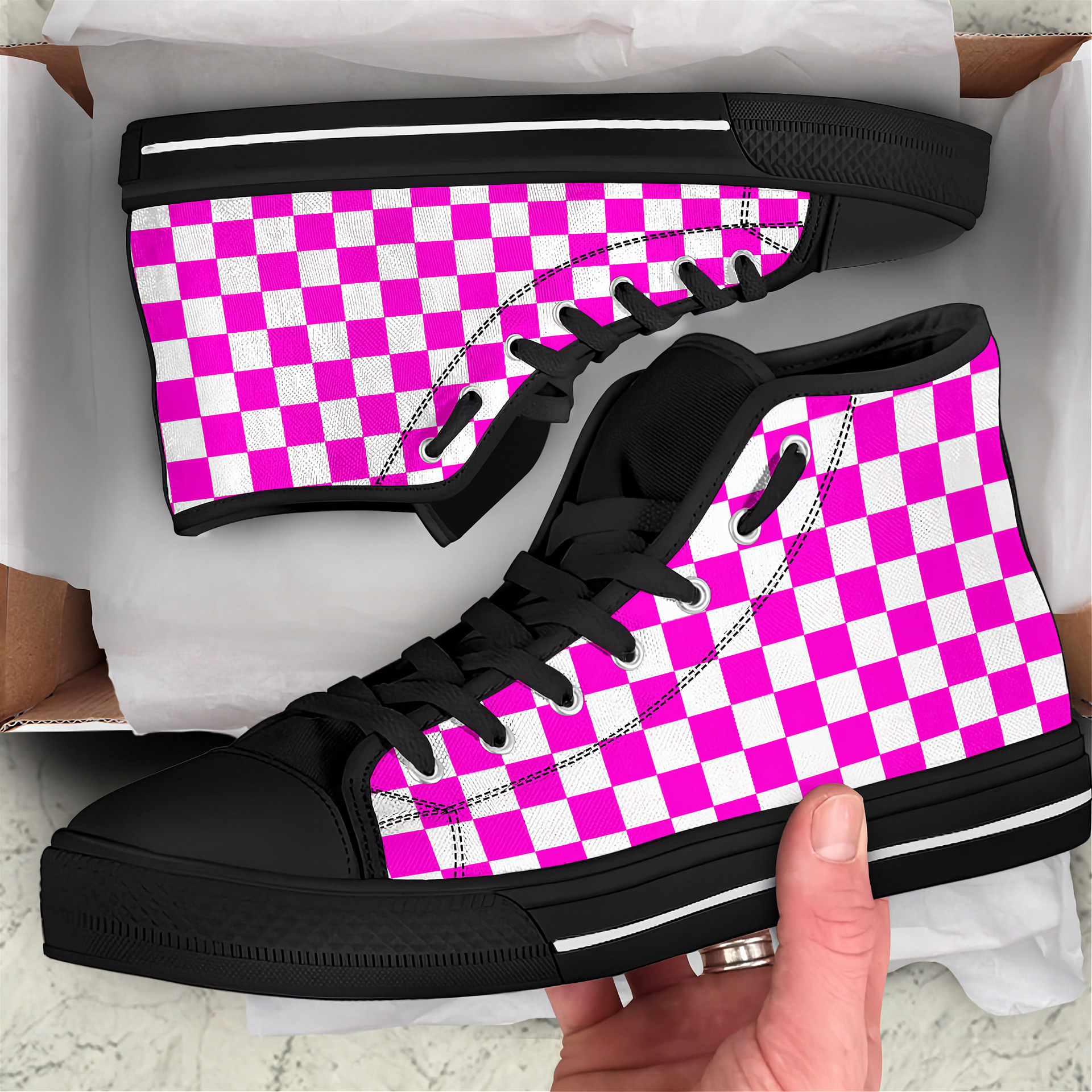 Black high-top sneakers with pink and white checkered pattern held by a hand.