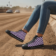 Person wearing purple and white checkered sneakers on a dirt track with cars in the background.