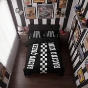 A racing-themed bedding set displayed on a bed in a styled bedroom. The set includes a black duvet cover and matching pillowcases with bold white text reading 'RACING QUEEN' and 'RACING KING' flanking a central black-and-white checkered stripe.