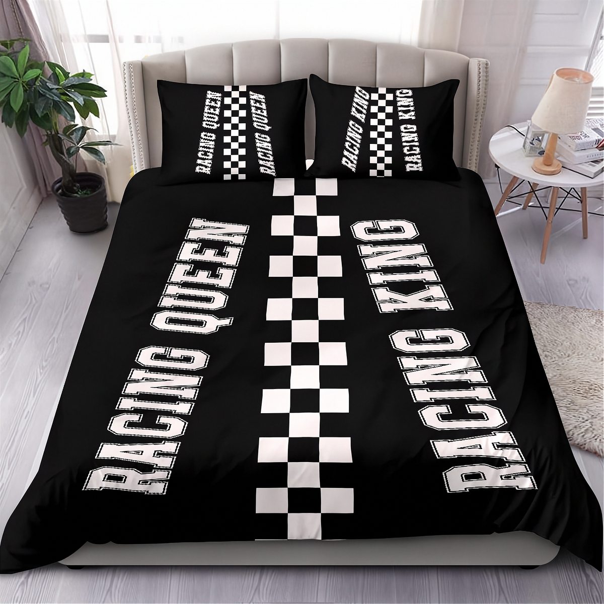 A black bedding set on a bed in a styled bedroom, featuring a duvet cover and two pillowcases with racing-themed graphics: large white 'RACING QUEEN' and 'RACING KING' text, and a central black-and-white checkered stripe pattern.