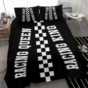 A black bedding set with a racing theme, featuring a duvet cover and two pillowcases with 'RACING QUEEN' and 'RACING KING' printed in white block letters alongside black-and-white checkered stripes, shown in a modern bedroom setting.