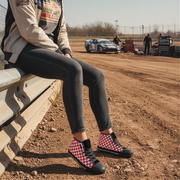 Person sitting on a tire at a race track wearing checkered shoes.