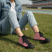 Person wearing red and white checkered sneakers on a grassy area with a race track in the background.
