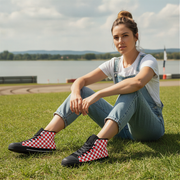 Woman sitting on grass wearing checkered shoes with a lake and sky in the background