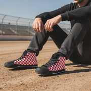 Person wearing black high-top shoes with red and white checkered pattern sitting on a dirt surface.
