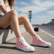 Person wearing red and white checkered high-top sneakers sitting on a concrete ledge with a race track in the background.