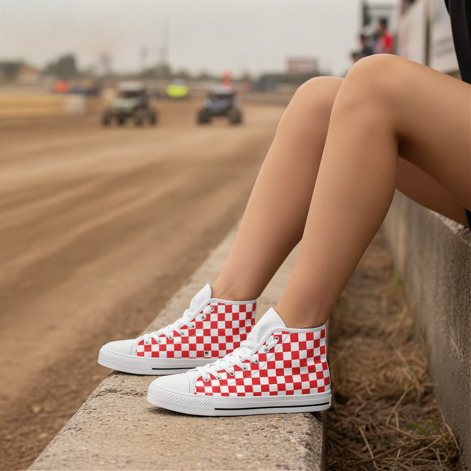 Red and white checkered shoes worn by a person sitting on a concrete ledge with a blurred dirt track background.