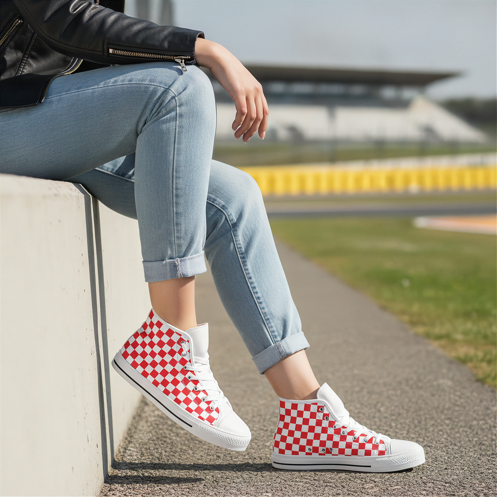 Person wearing red and white checkered high-top shoes sitting on a concrete ledge with a race track in the background.