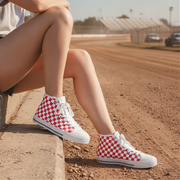 Person wearing red and white checkered high-top shoes sitting on a curb with a race track in the background.