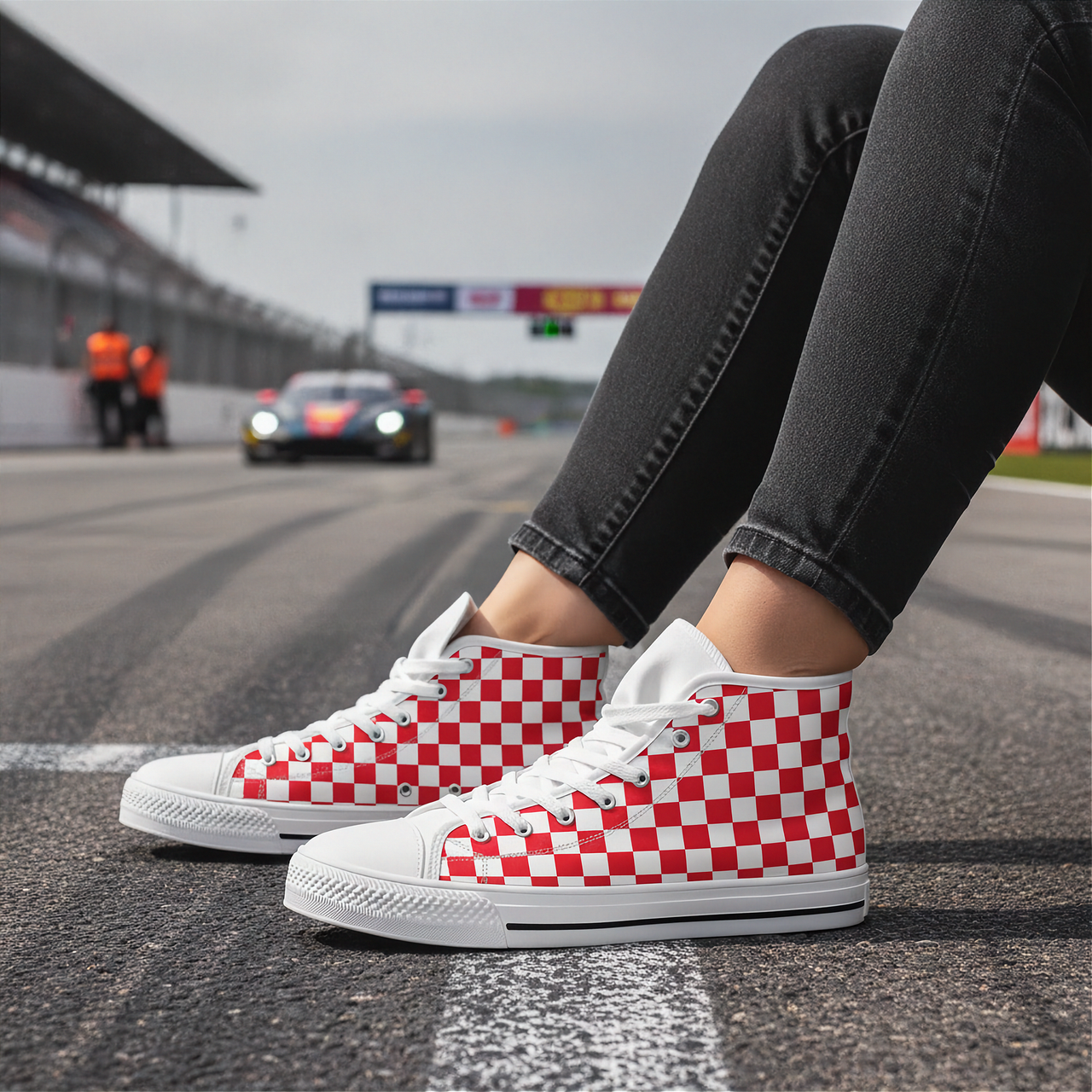 Red and white checkered shoes worn on a race track with cars in the background.