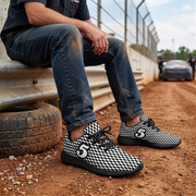 A person sitting on a metal track barrier wearing black and white checkered sneakers with a large white number 5 on the side, paired with blue jeans in a dirt racing environment.