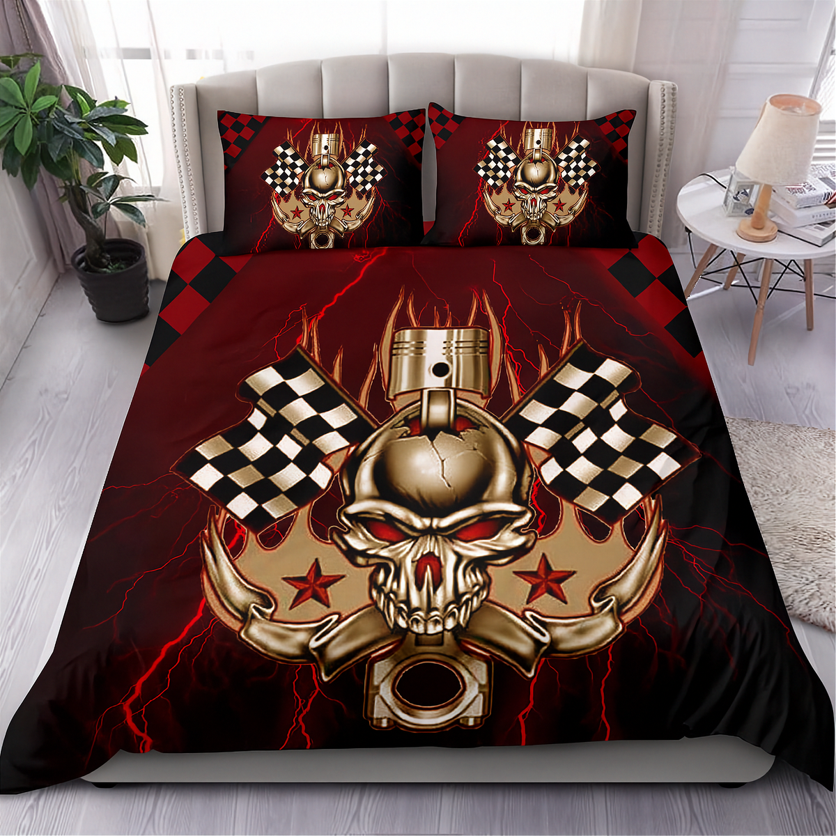 A bed dressed in a bold black and red graphic bedding set featuring a large metallic gold skull with a piston, crossed checkered flags, lightning, and red stars. Two matching pillowcases are placed at the head of the bed in a styled bedroom with a plant, side table, lamp, and light wood floor.